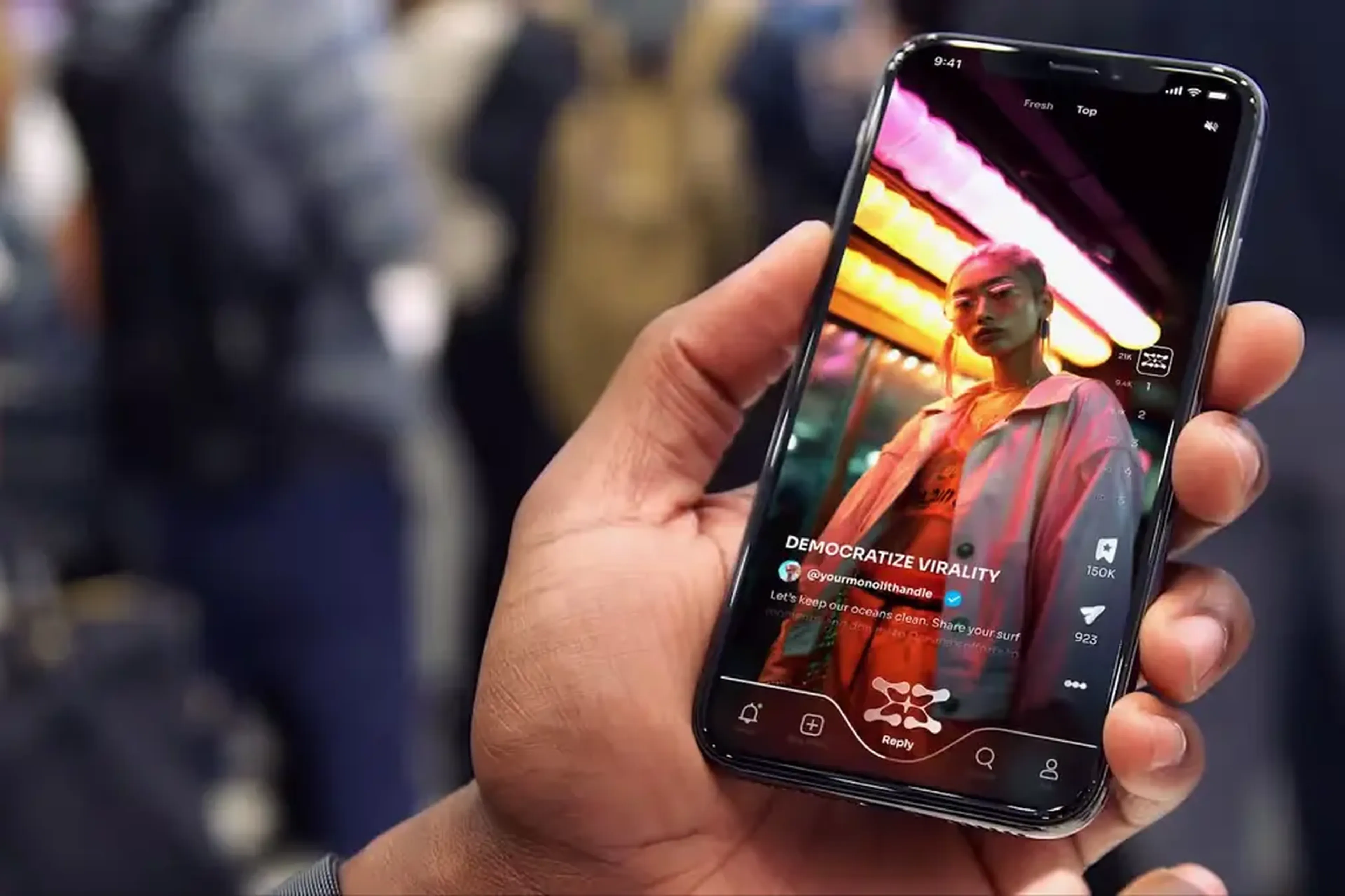 Person holding a smartphone displaying a social media app with a photo of a person in a pink jacket, overlaid with vibrant neon lights.