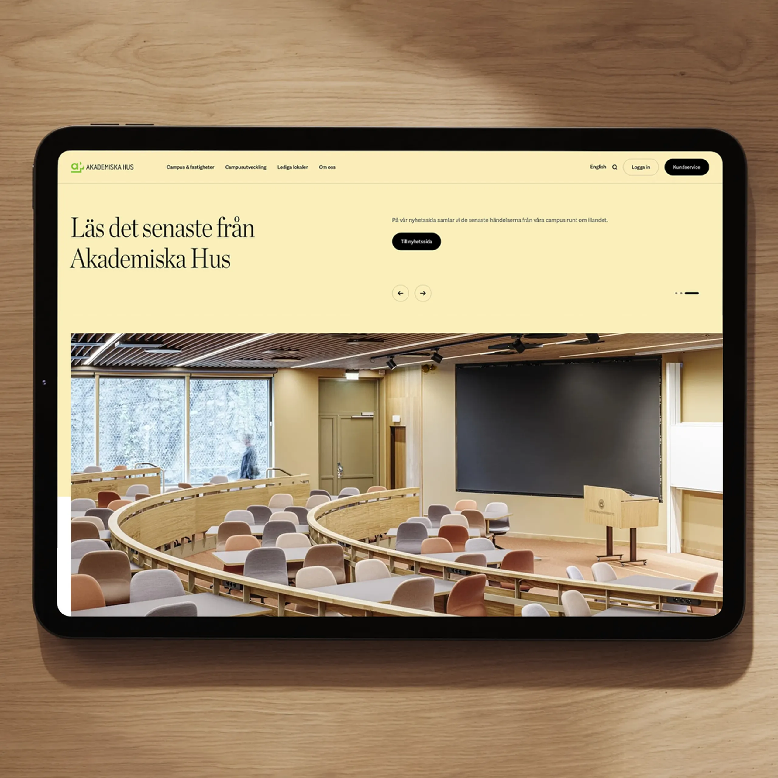 Akademiska Hus news page on a tablet, with a photo of a tiered lecture hall.