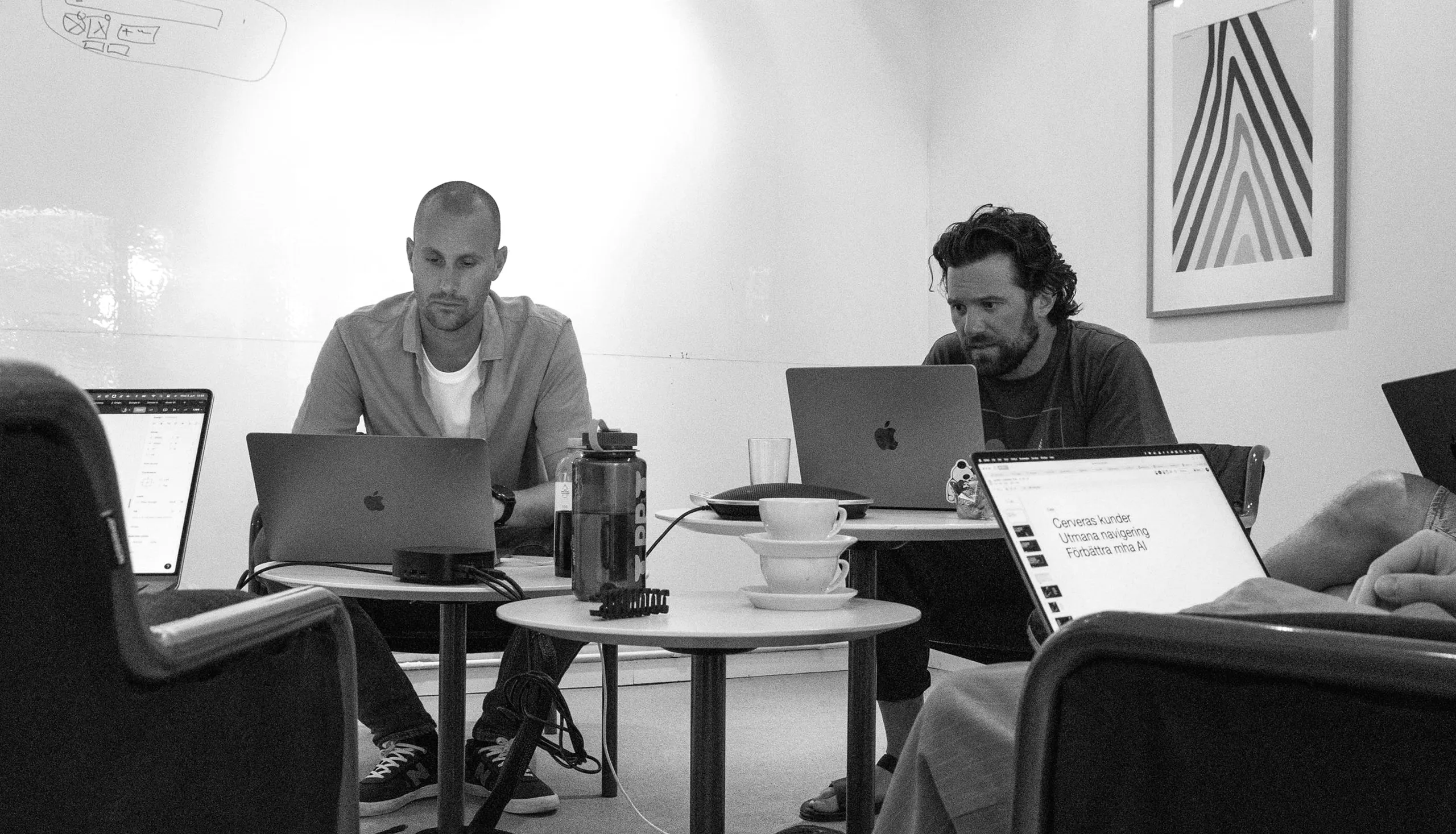 Colleagues working on laptops around small tables in a meeting room.