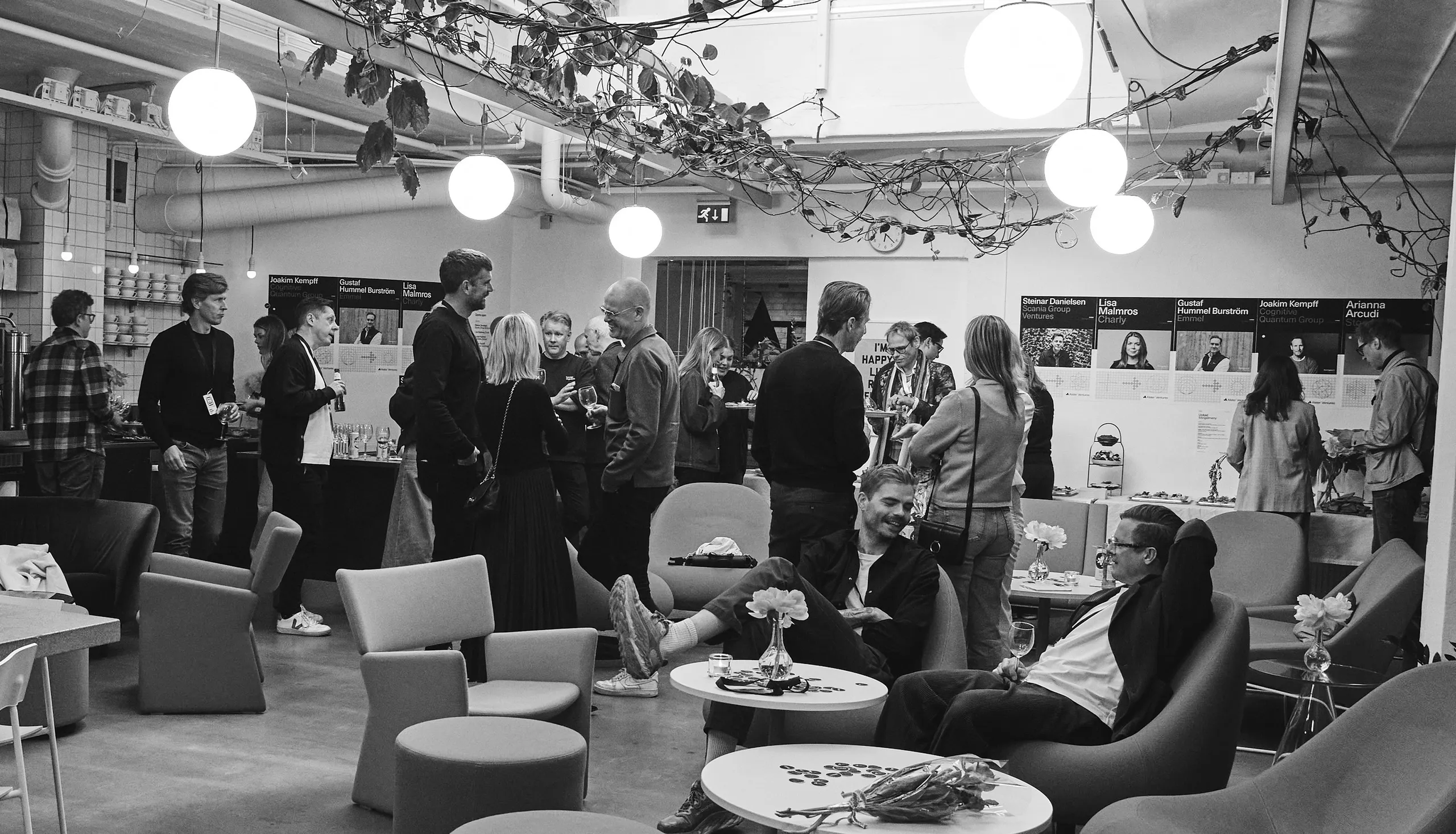 Guests mingling at an Alster Ventures event, with lounge chairs, hanging globe lights and speaker posters.